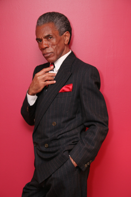 andre de shields wearing suit in front of red background