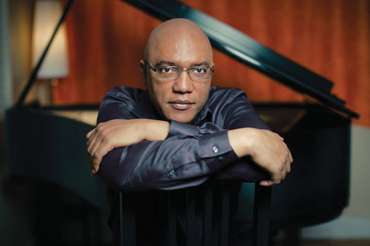 A person with a black dress shirt sitting on a chair in front of a grand piano.
