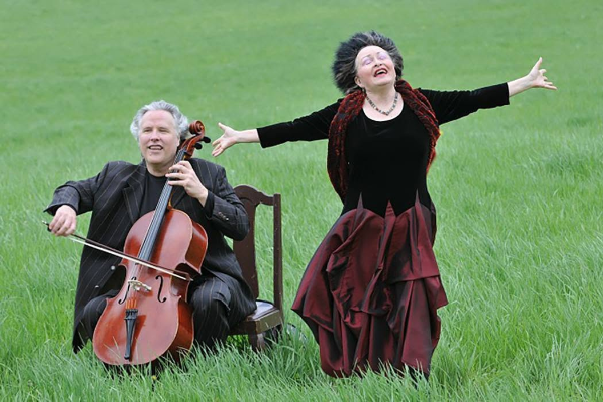 A cellist and singer performing in a field of grass.