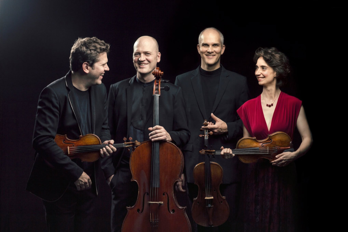 Photo of a string quartet looking at each other and smiling.