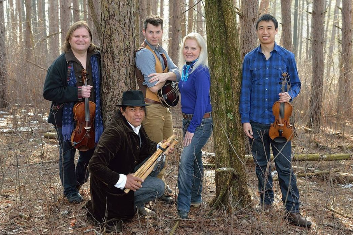 Five people standing in a forest, holding their instruments.