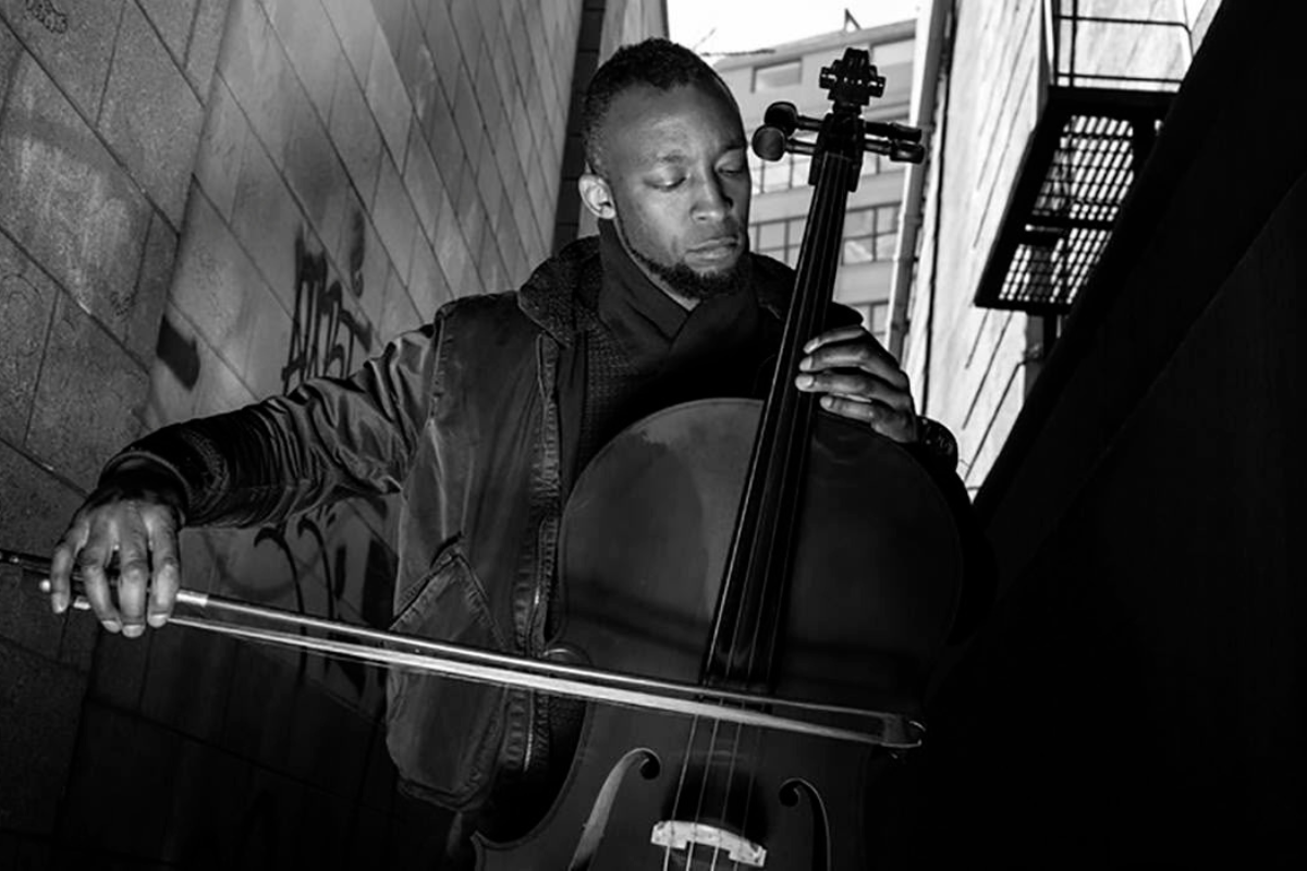 Black and white photo of a person playing the cello in an alleyway.