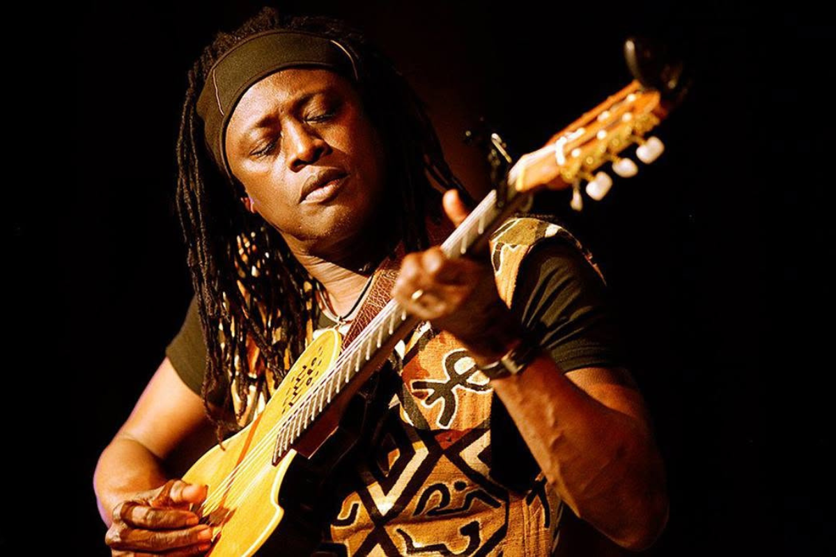 A person playing a guitar in front of a black background.
