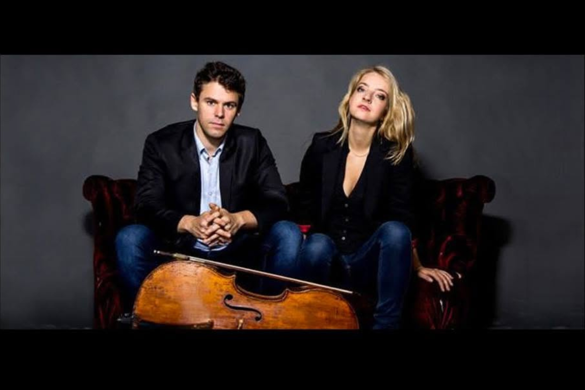 Two people wearing formal clothing, sitting down in front of a cello.