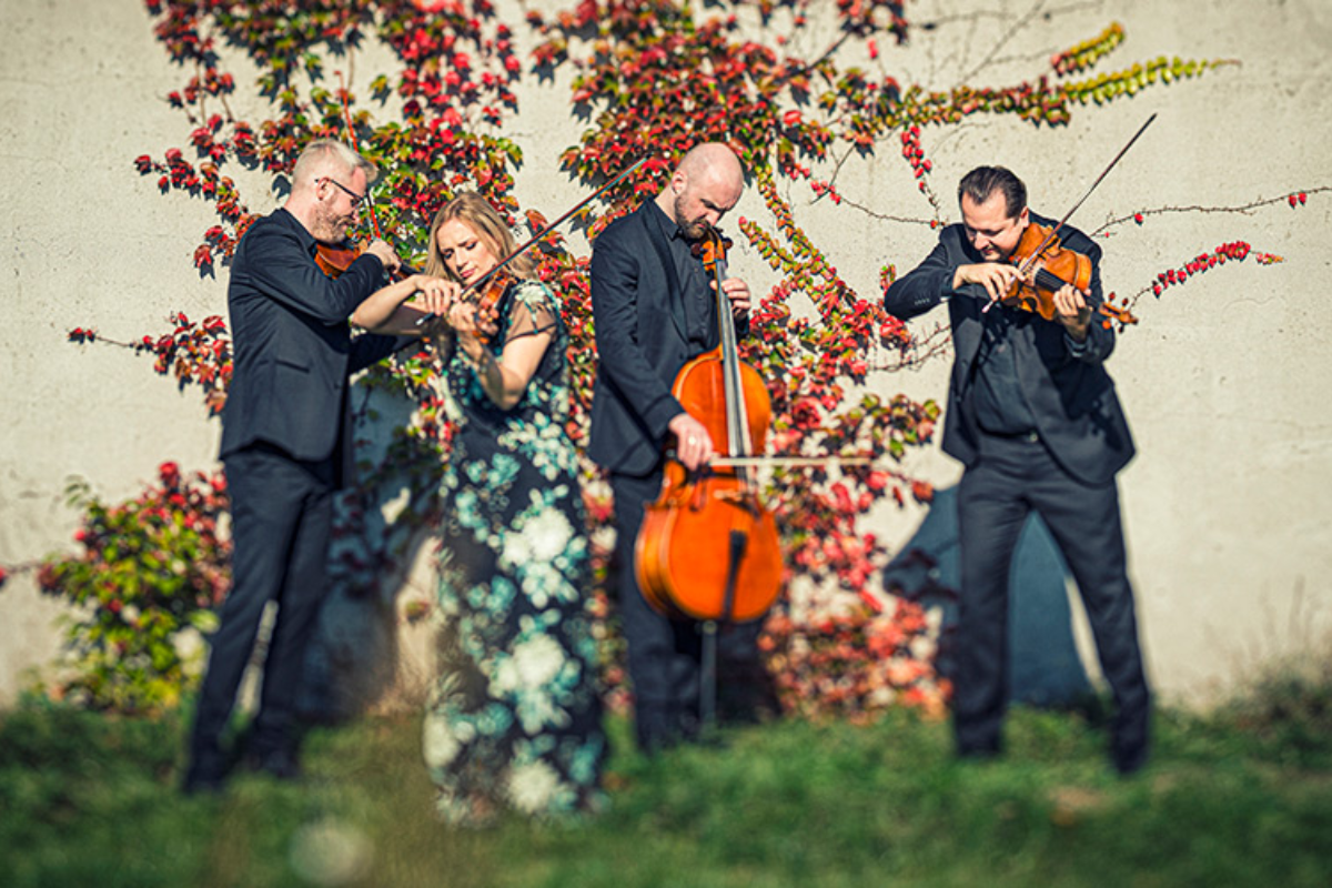 Meccore String Quartet standing outdoors, playing their instruments.