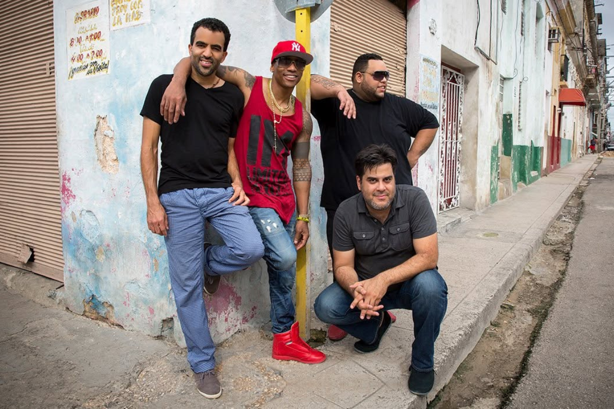 A group of four leaning on each other and smiling on a street corner.