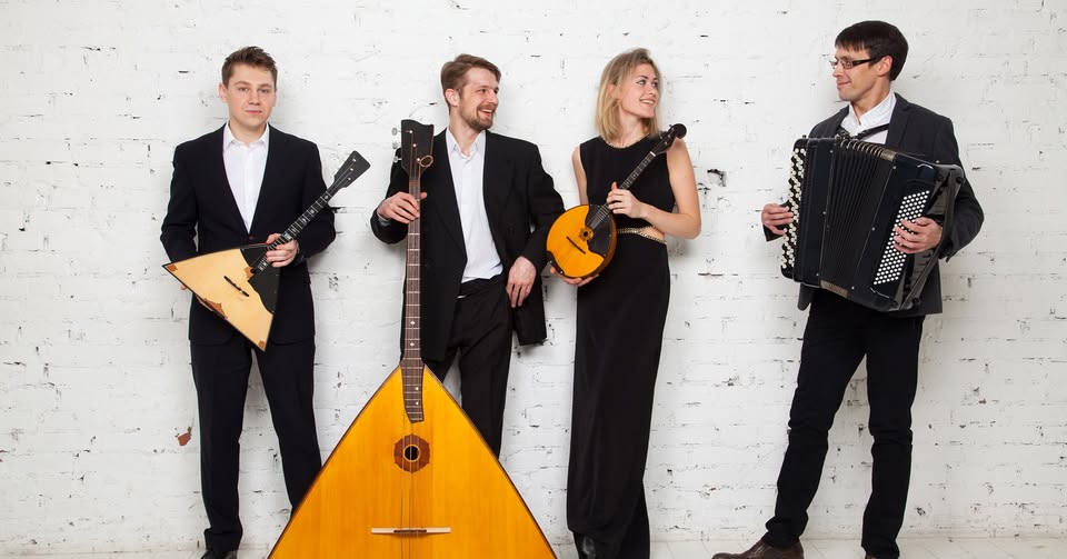 A quartet dressed in formal attire holding their instruments and looking at each other, laughing.