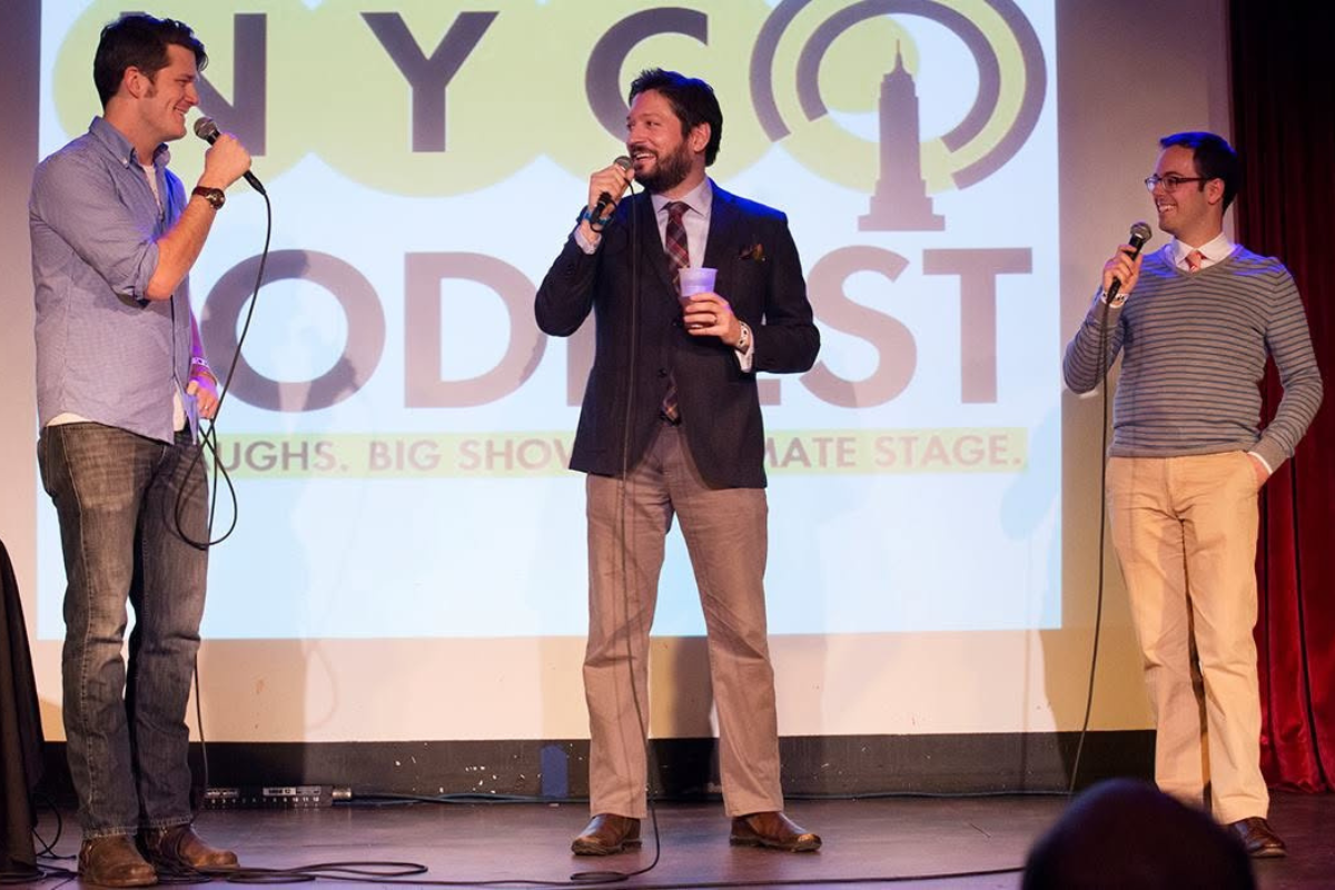 Three people standing on stage with wired microphones, talking.