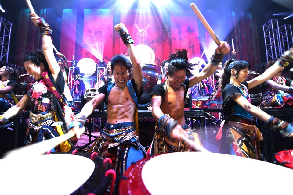 A group of taiko drummers on stage, hitting their drums.