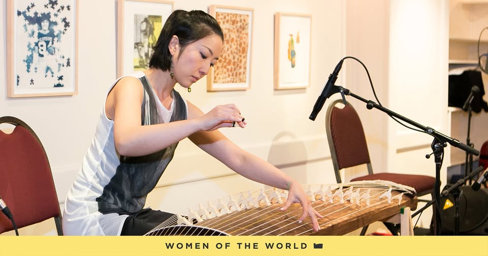 A person plays a tabletop string instrument in a recording studio.