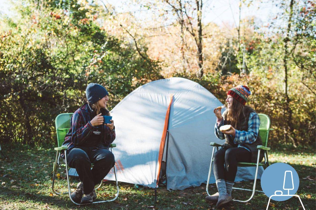 Two people sit in chairs in front of a tent