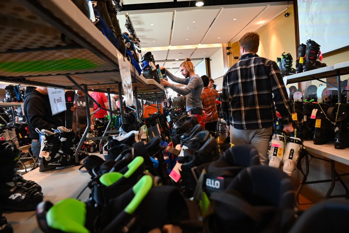 Individuals shopping down aisles of ski boots and winter gear.