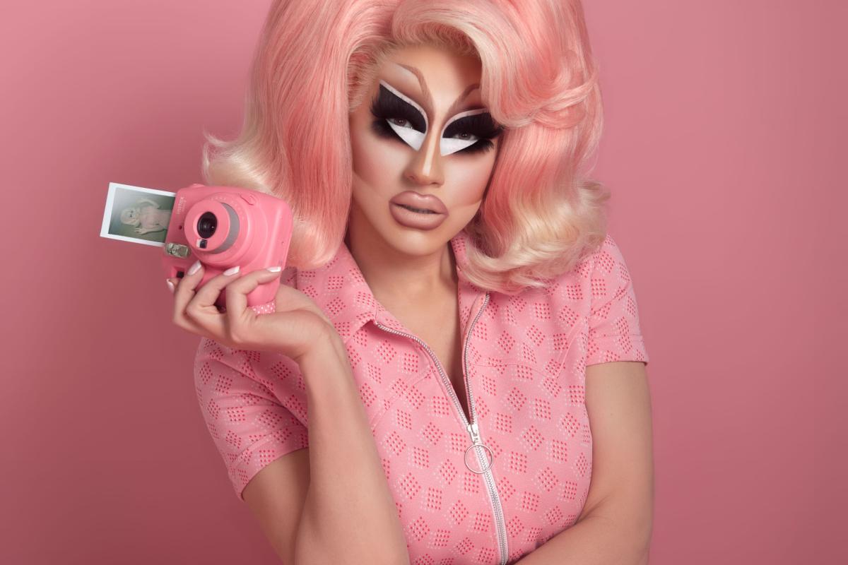 Trixie Mattel dressed in pink holding a pink Polaroid camera.