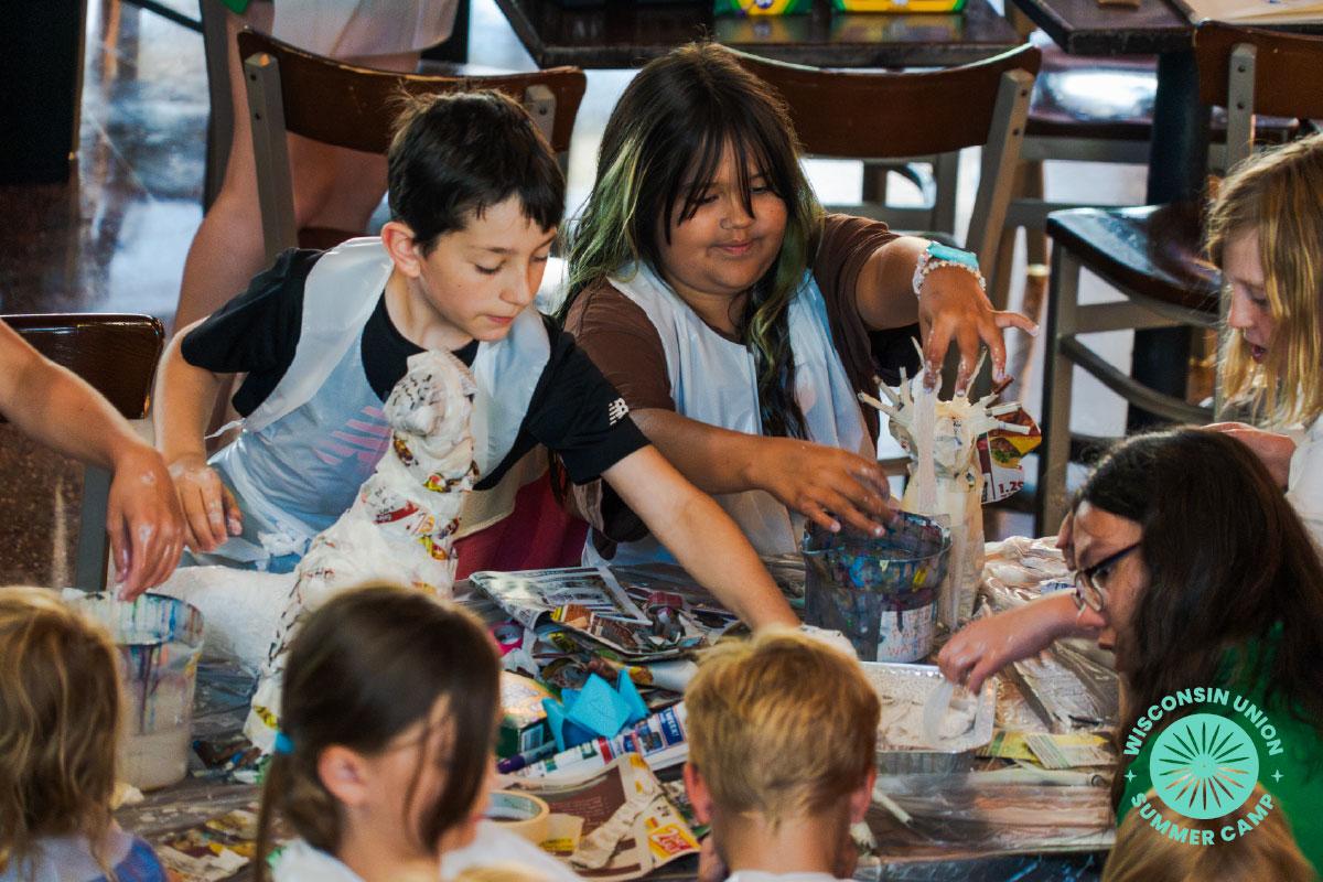 children sitting around a table, smiling, and working on paper mache.