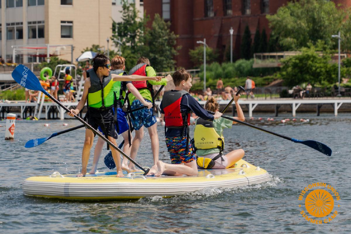 Group of children on a large stand up paddleboard.