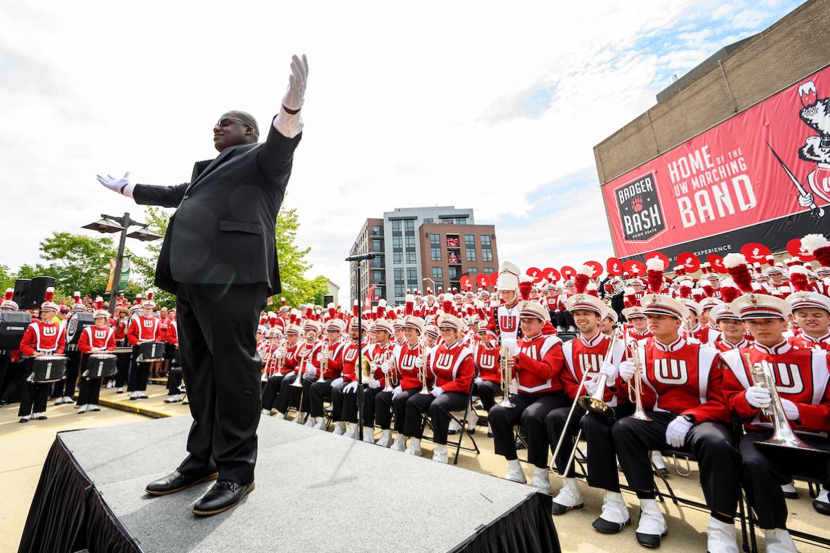 Corey Pompey standing up on stage at Badger Bash, with UW Marching Band behind him.