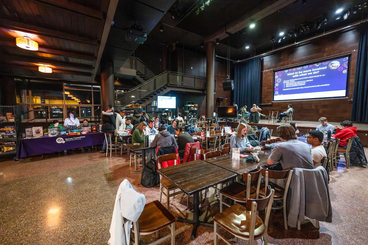Students sitting at tables and playing board games and video games together.