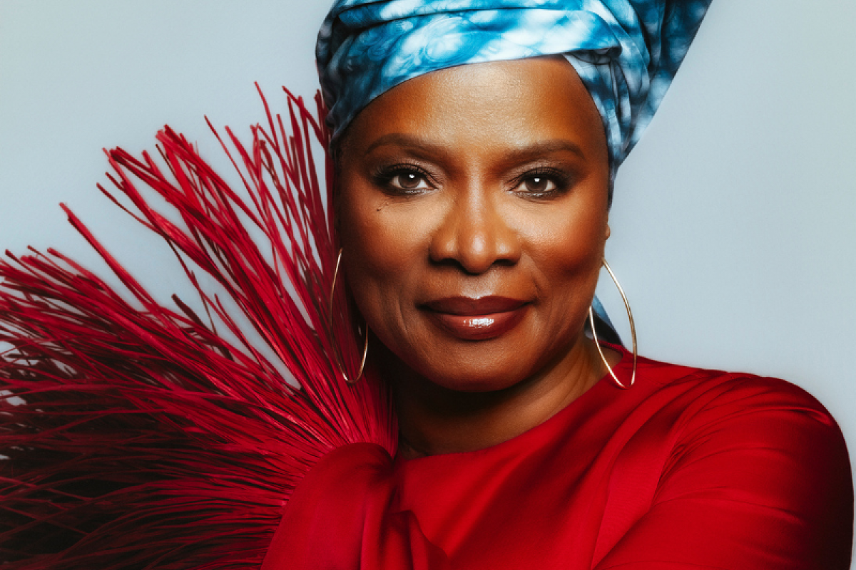Angelique Kidjo standing in front of a light blue background.