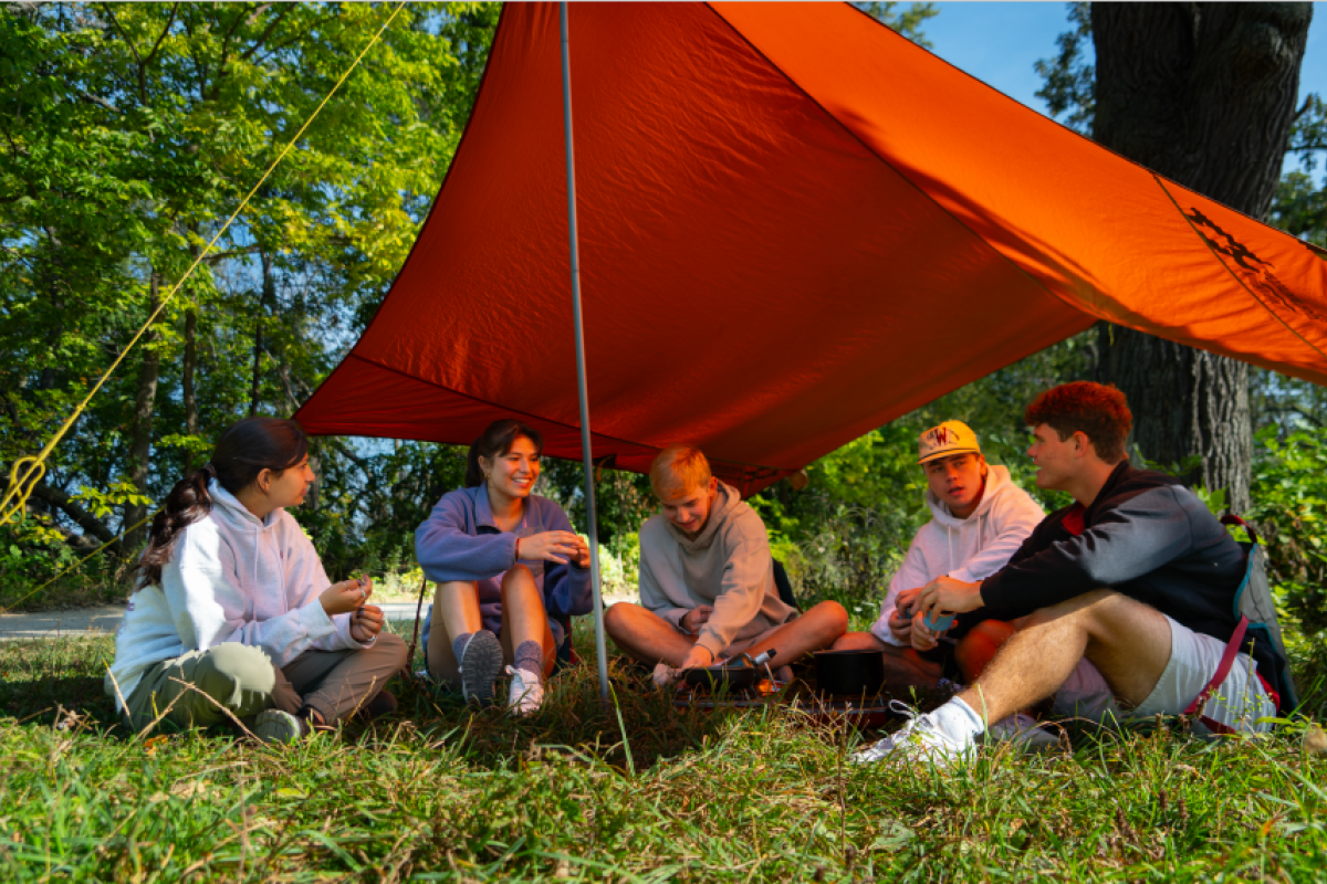 Students sitting under a tent and talking.