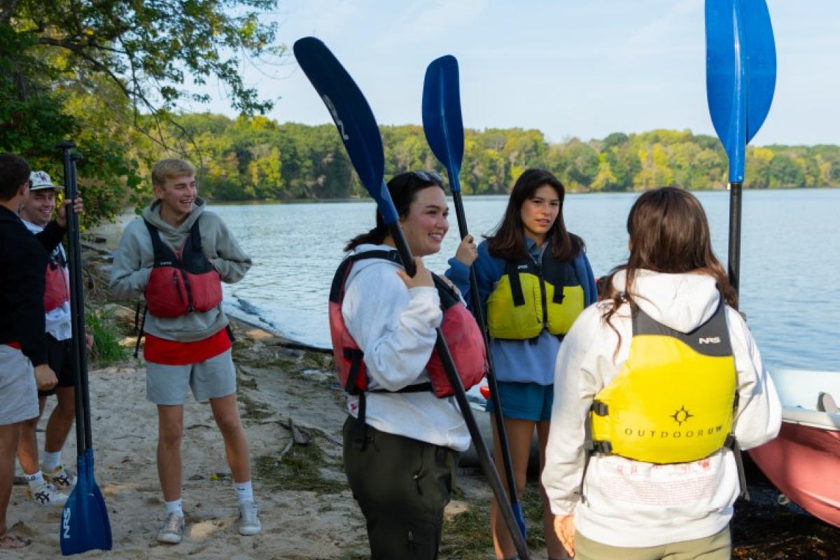 Students standing on the shores of Picnic Point with kayak paddles.