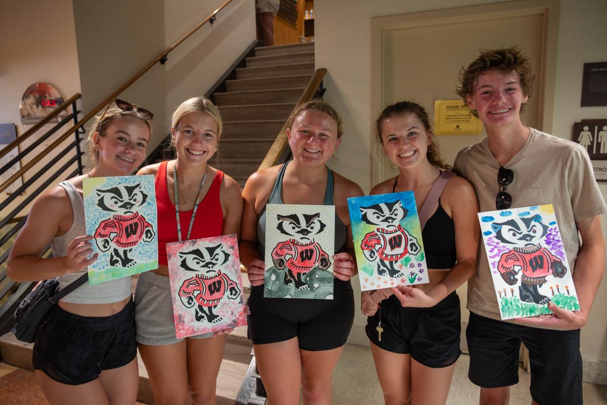 Photo of five students holding up watercolor paintings of Bucky the Badger.