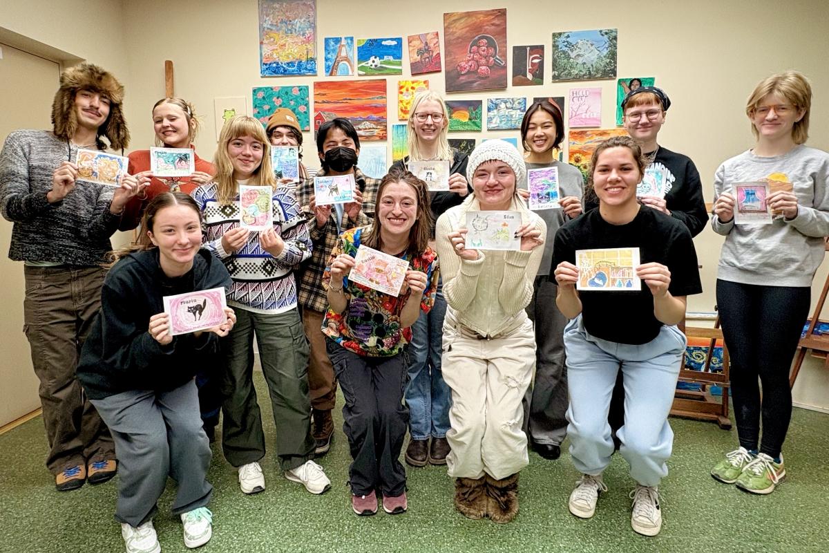 Photo of a group each holding up paintings.