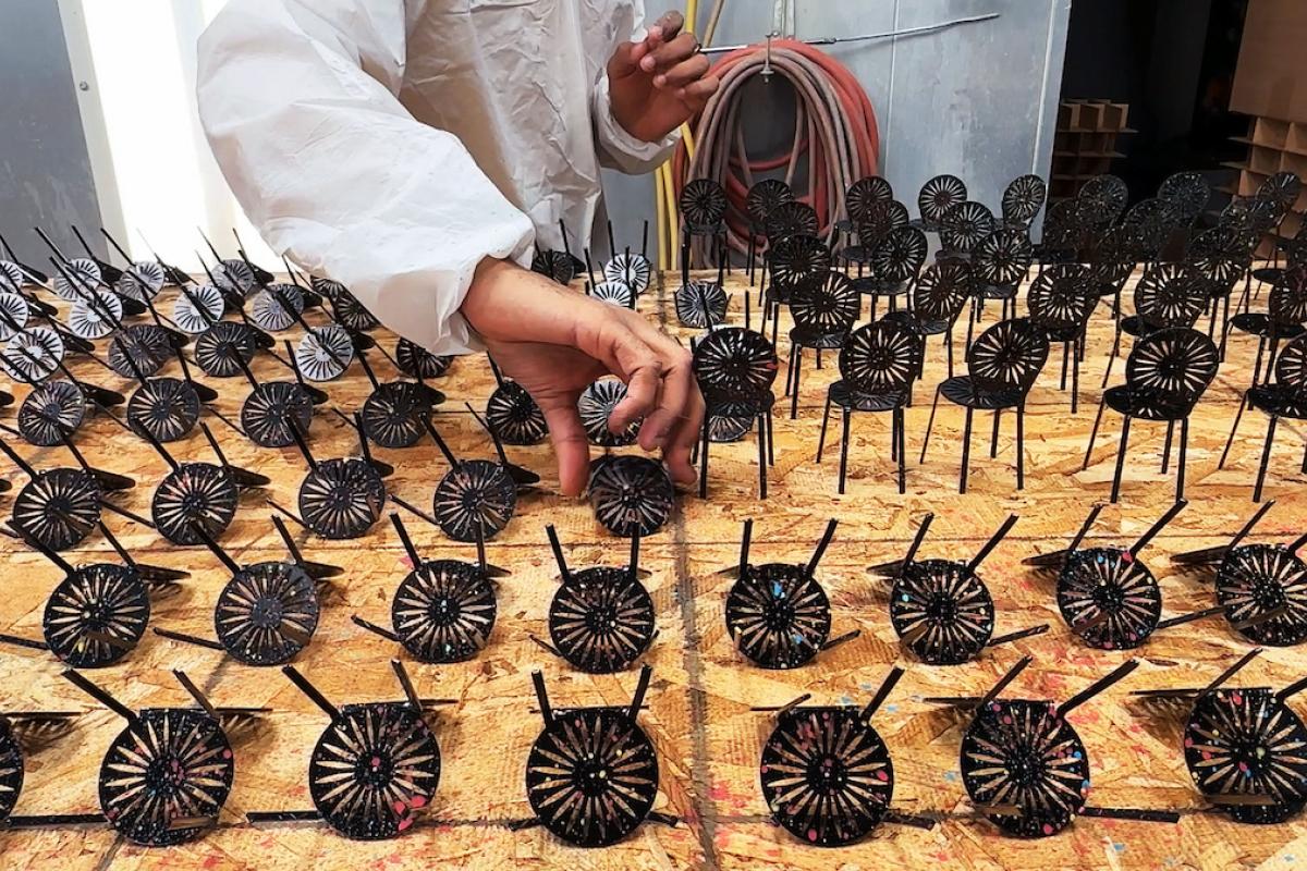 A person in a white smock lays out freshly-painted mini Terrace chairs to dry