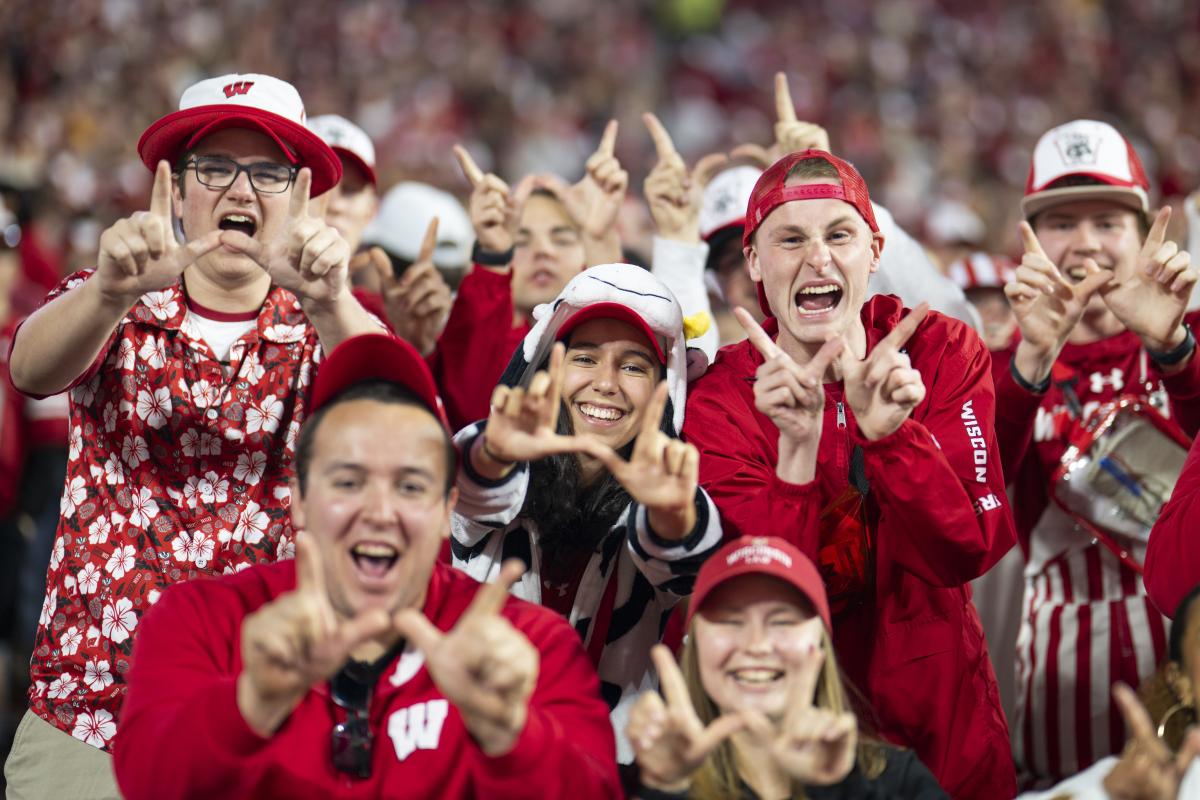 A group of UW–Madison fans cheering at the sidelines of a football game.