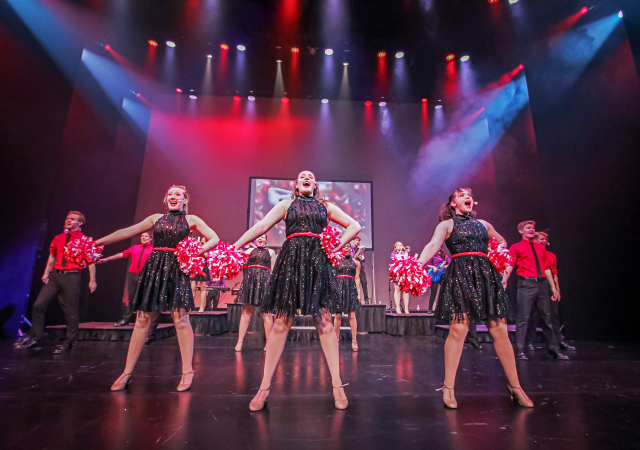 Wisconsin Singers pose on stage under stage lights wearing black and red costumes