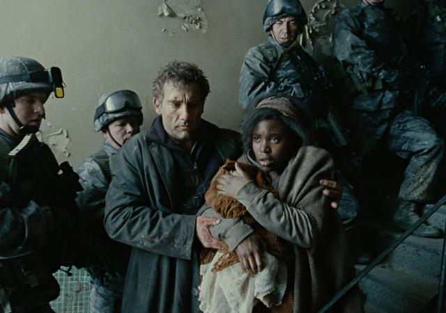 Still from film Children of Men. man and woman stand surrounded by military officers.