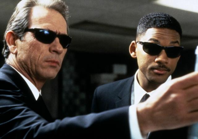 Image from film Men in Black, two men in suits and sunglasses hold memory eraser device.