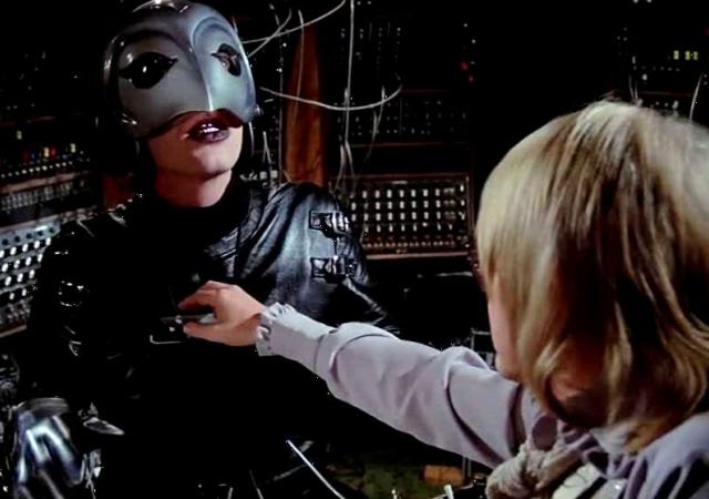 Still from film Phantom of the Paradise, person in beak-like mask stares at another person.