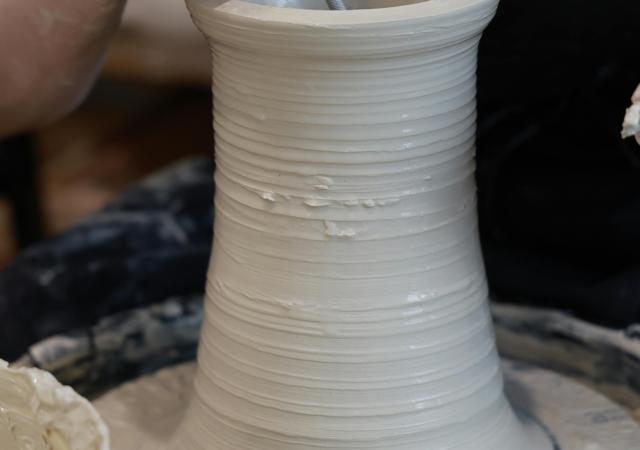 Hands working on a tall ceramic vase.