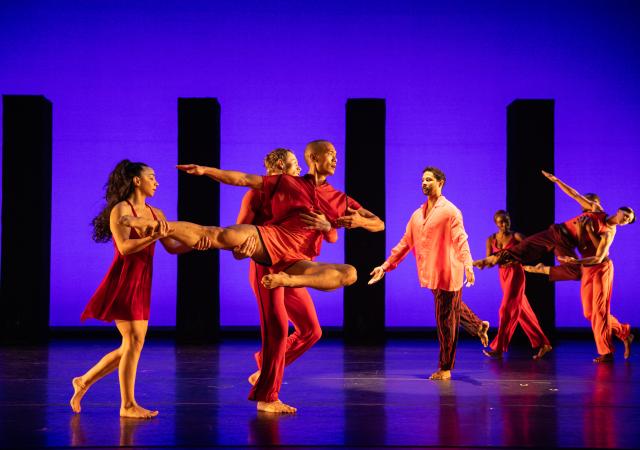 Dancers in red in a pose in front of purple background.