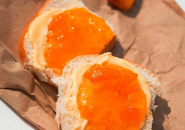 A peach jam sandwich on brown paper with slices of peaches