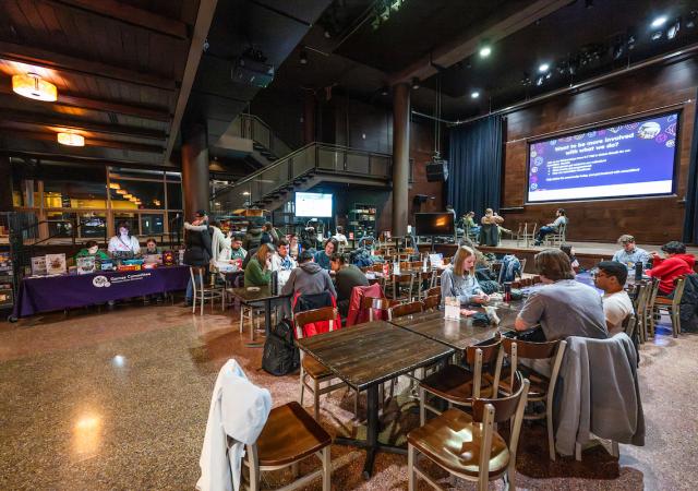 Students sitting at tables and playing board games and video games together.