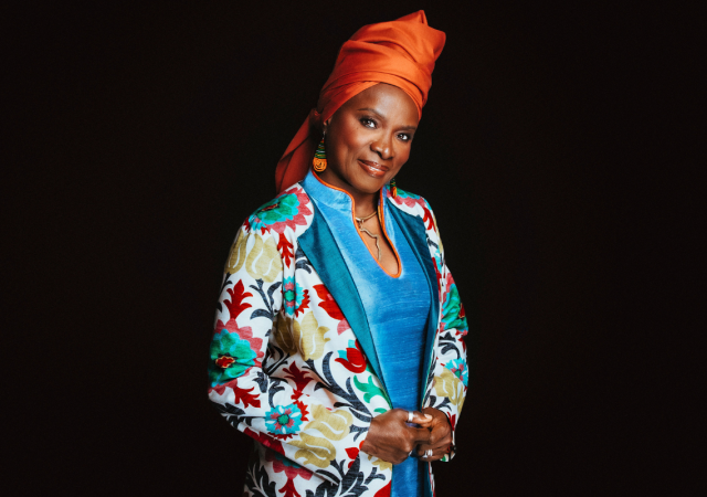 Angelique Kidjo standing in front of a black background.