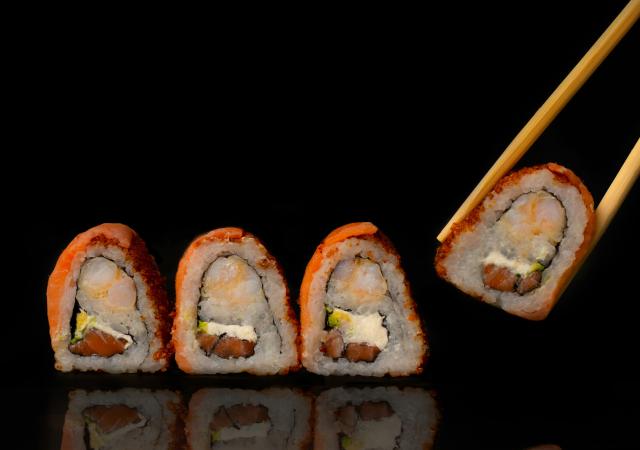 Sushi being held by a pair of chopsticks with more sushi on table