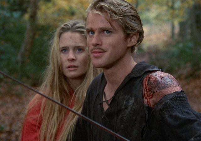 woman in red standing to the left of man in black holding a thin sword