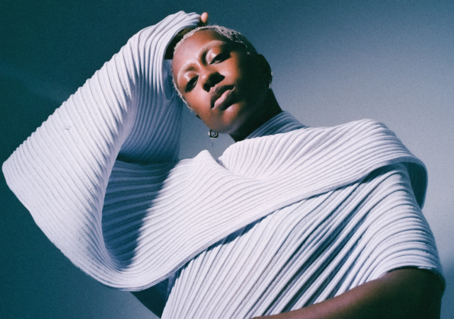 anaiis standing in front of a white and blue backdrop.