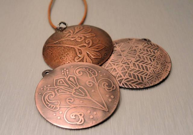 Photo of three necklace pendants that are copper etched.