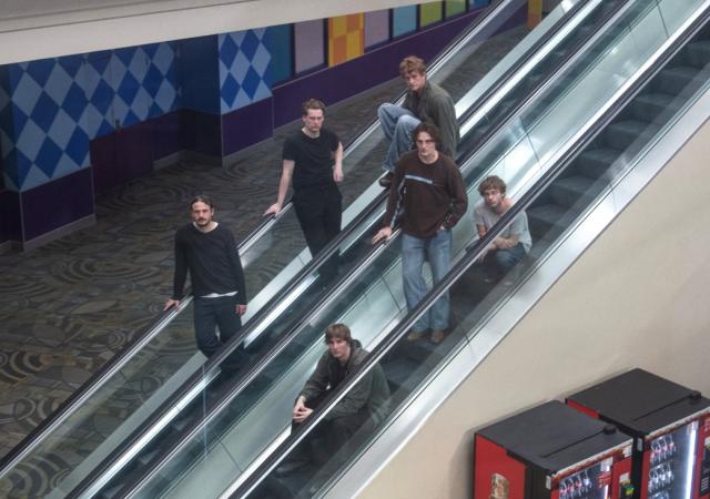 The six-piece band Dutch Interior poses for a photo on 2 escalators.