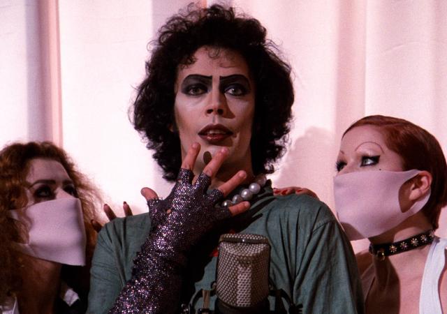 Individual in spooky makeup looks shocked, two individuals in surgical masks look at them.