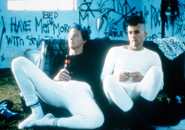 Two individuals with punk style sitting in a graffiti-filled room with beers.