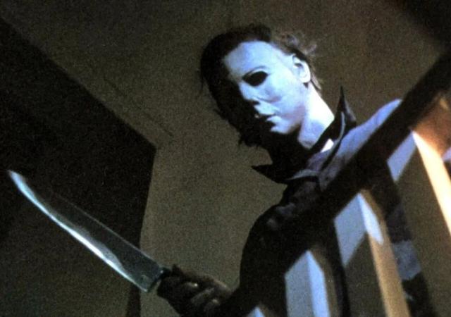 individual in a creepy mask looks down a stairwell with a knife in hand