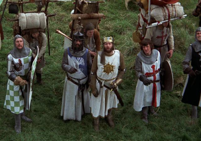 5 individuals dressed as medival knights looking up, with sheilds and swords.