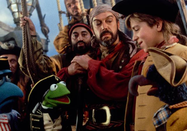Muppets in pirate uniforms on a boat with 3 individuals also dressed as pirates.