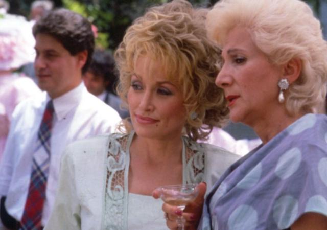 Two older women gossip at an outdoor party with pastel decor
