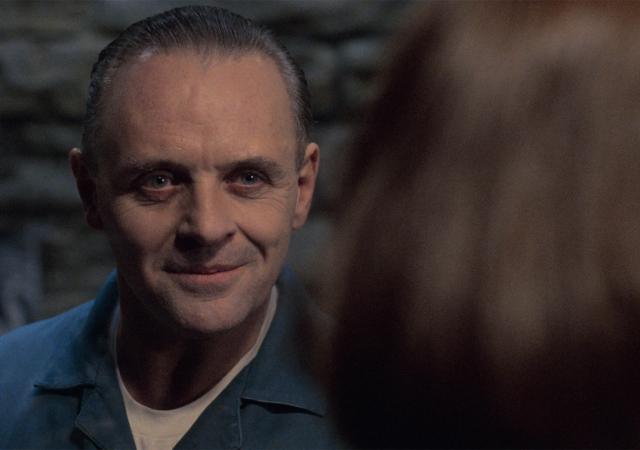 man in prison blue jumpsuit smiling creepily at a woman.