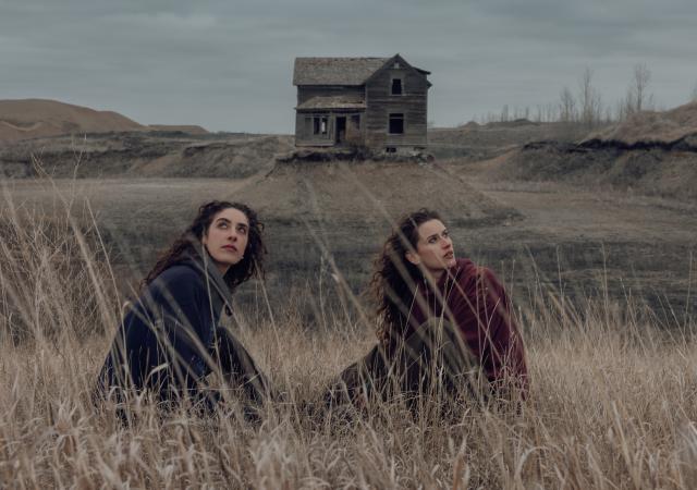 Tommy Lefroy duo sitting in a field of dried grass with a house far behind.